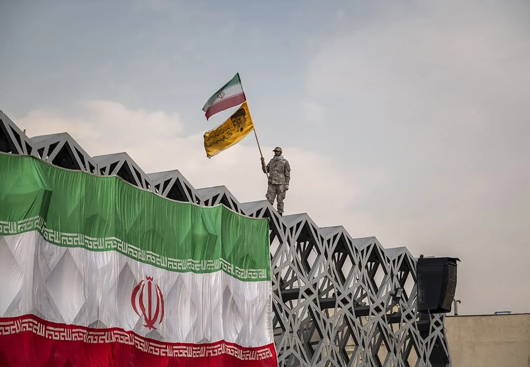 Un miembro del Cuerpo de la Guardia Revolucionaria Islámica (IRGC) ondea una bandera de Irán y una bandera con un retrato del Líder Supremo de Irán, el Ayatolá Ali Khamenei, mientras está de pie sobre una bandera gigante de Irán durante una manifestación en la plaza Imam Hussein en el sureste de Teherán el 30 de diciembre de 2021. Seguidores del Líder Supremo de Irán, el Ayatolá Ali Khamenei, asisten a una manifestación para conmemorar el aniversario de las manifestaciones contra la oposición de diciembre de 2009 en Teherán. (Foto por Morteza Nikoubazl/NurPhoto) PROHIBIDO USO EN FRANCIA
