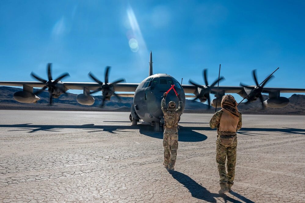 El Sargento Técnico de la Fuerza Aérea de los EE. UU. Nathaniel Deloatch, izquierda, y el Sargento Maestro Austin Schaffer, ambos controladores de tráfico aéreo asignados al Escuadrón de Apoyo a Operaciones 57, guían un EC-130 Compass Call asignado al 55º Grupo de Combate Electrónico en apoyo al entrenamiento de Punto de Armamento y Reabastecimiento Avanzado en Delamar Dry Lake, Nevada, el 30 de octubre de 2025. (Foto de la Fuerza Aérea de los EE. UU. por la Aviadora de Primera Clase Heather Amador)
