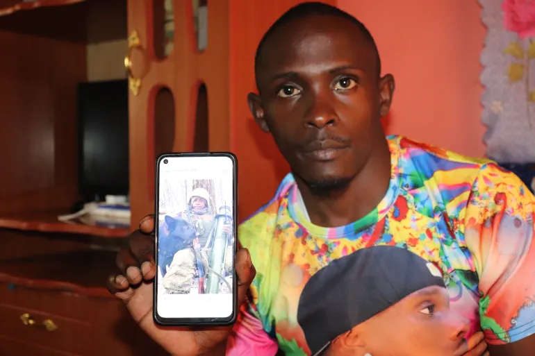 DancanChege muestra una foto de sí mismo en Ucrania con equipo de combate completo, luchando por Rusia el año pasado./ Créditos: Dominic Kirui/Al Jazeera.