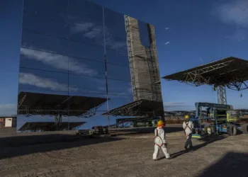 Workers pass in front of a heliostat panel at the Cerro Dominador Solar Thermal Plant in the Atacama desert in the commune of Maria Elena, Antofagasta region, Chile, on Wednesday, Aug. 1, 2018. Cerro Dominador, South America's only solar-thermal project, will be a breathtaking piece of engineering, with 10,800 giant mirrors focusing light to the top of a tower more than twice the height of the Statue of Liberty. Photographer: Cristobal Olivares/Bloomberg 