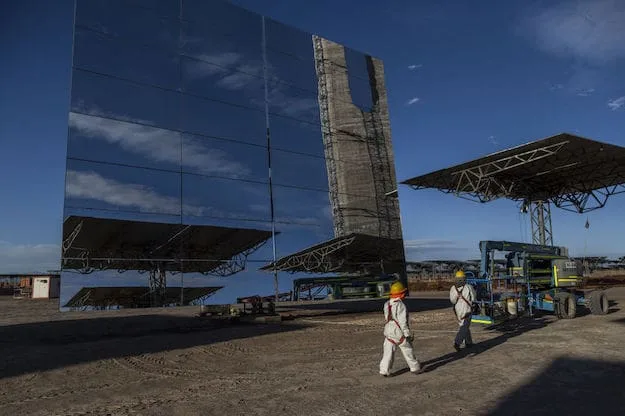 Workers pass in front of a heliostat panel at the Cerro Dominador Solar Thermal Plant in the Atacama desert in the commune of Maria Elena, Antofagasta region, Chile, on Wednesday, Aug. 1, 2018. Cerro Dominador, South America's only solar-thermal project, will be a breathtaking piece of engineering, with 10,800 giant mirrors focusing light to the top of a tower more than twice the height of the Statue of Liberty. Photographer: Cristobal Olivares/Bloomberg