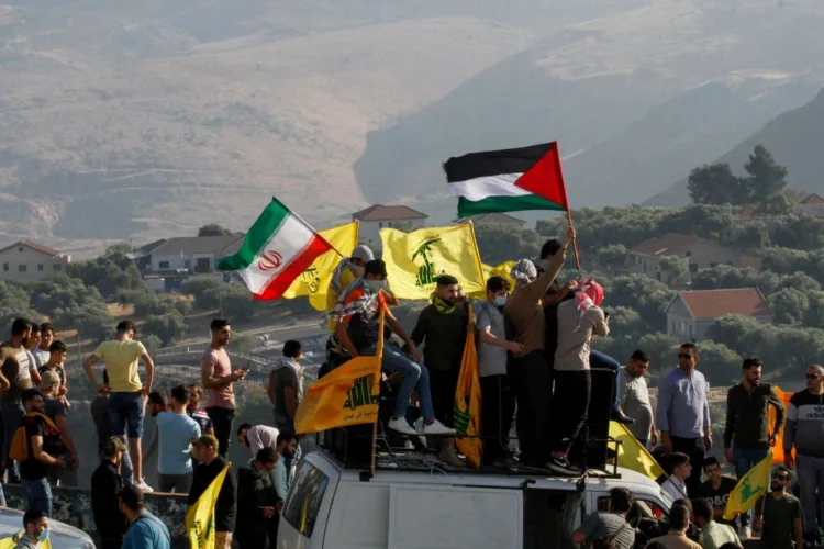 (FILES) In this file photo taken on May 14, 2021 Supporters of Lebanon's Hezbollah lift its flags (C) alongside those of Iran (L) and Palestine, during an anti-Israel protest in the southern Khiam area by the border with Israel, facing the northern Israeli town of Metula. - Israel's deadly Gaza offensive has many eyes trained on the Lebanese border for a Hezbollah reaction but observers argue the Iran-backed movement is unlikely to risk an all-out conflict. Hezbollah and the Palestinian Hamas, both designated as terrorist groups by Israel and much of the West, have mended fences after ending up on opposing sides of the Syrian war a decade ago. (Photo by Mahmoud ZAYYAT / AFP)