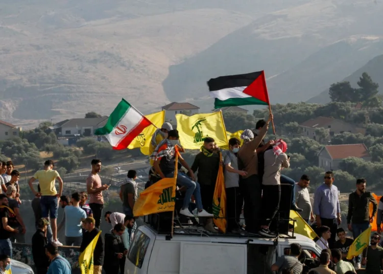 (FILES) In this file photo taken on May 14, 2021 Supporters of Lebanon's Hezbollah lift its flags (C) alongside those of Iran (L) and Palestine, during an anti-Israel protest in the southern Khiam area by the border with Israel, facing the northern Israeli town of Metula. - Israel's deadly Gaza offensive has many eyes trained on the Lebanese border for a Hezbollah reaction but observers argue the Iran-backed movement is unlikely to risk an all-out conflict. Hezbollah and the Palestinian Hamas, both designated as terrorist groups by Israel and much of the West, have mended fences after ending up on opposing sides of the Syrian war a decade ago. (Photo by Mahmoud ZAYYAT / AFP)