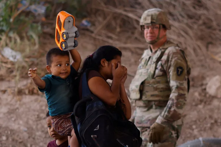 Migrants stand near the Rio Bravo river after crossing the border to, request asylum in the United States, as a member of the Texas Army National Guard stands guard to inhibit migrants crossing, as seen from Ciudad Juarez, Mexico May 13, 2023. REUTERS/Jose Luis Gonzalez