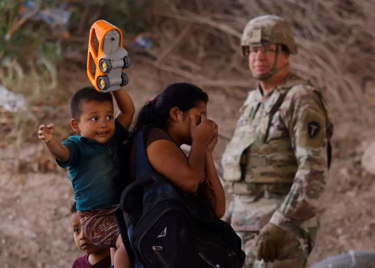 Migrants stand near the Rio Bravo river after crossing the border to, request asylum in the United States, as a member of the Texas Army National Guard stands guard to inhibit migrants crossing, as seen from Ciudad Juarez, Mexico May 13, 2023. REUTERS/Jose Luis Gonzalez
