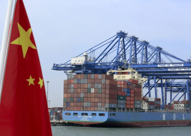 A Chinese flag flies on a vessel moving past shipping containers being unloaded at a Tianjin Port Group Co. dock in Tianjin, China, on Wednesday, Sept. 12, 2012. The Chinese government is trying to meet a 7.5 percent economic growth target set in March, which would already be the weakest expansion since 1990. Photographer: Nelson Ching/Bloomberg