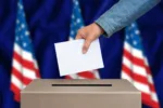 Presidential election in United States of America. The hand of woman putting her vote in the ballot box. American flags on background.
