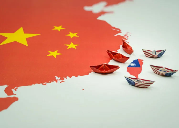 Paper boats with the colors of the USA and China surrounding the island of taiwan on a map. China and taiwan wat and conflict concept.