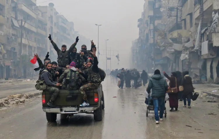Syrian pro-regime fighters, gesture as they drive past residents fleeing violence in the restive Bustan al-Qasr neighbourhood, in Aleppo's Fardos neighbourhood on December 13, 2016, after regime troops retook the area from rebel fighters. 
Syrian rebels withdrew from six more neighbourhoods in their one-time bastion of east Aleppo in the face of advancing government troops, the Syrian Observatory for Human Rights said. / AFP PHOTO / STRINGER