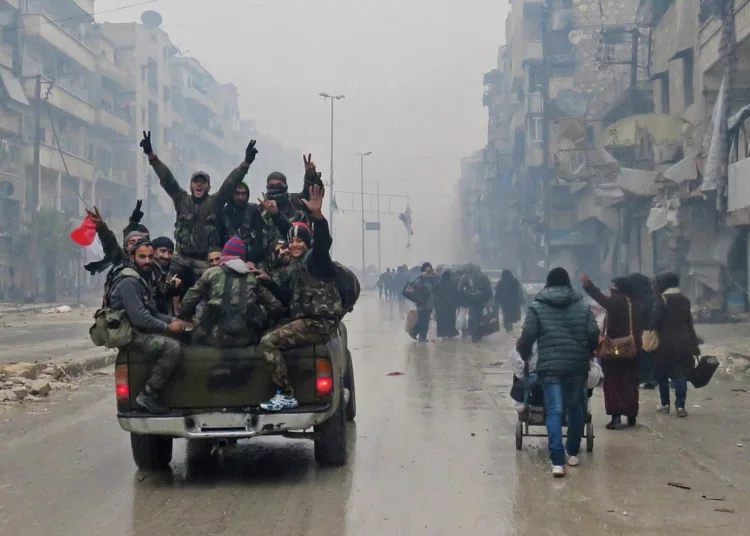 Syrian pro-regime fighters, gesture as they drive past residents fleeing violence in the restive Bustan al-Qasr neighbourhood, in Aleppo's Fardos neighbourhood on December 13, 2016, after regime troops retook the area from rebel fighters. 
Syrian rebels withdrew from six more neighbourhoods in their one-time bastion of east Aleppo in the face of advancing government troops, the Syrian Observatory for Human Rights said. / AFP PHOTO / STRINGER