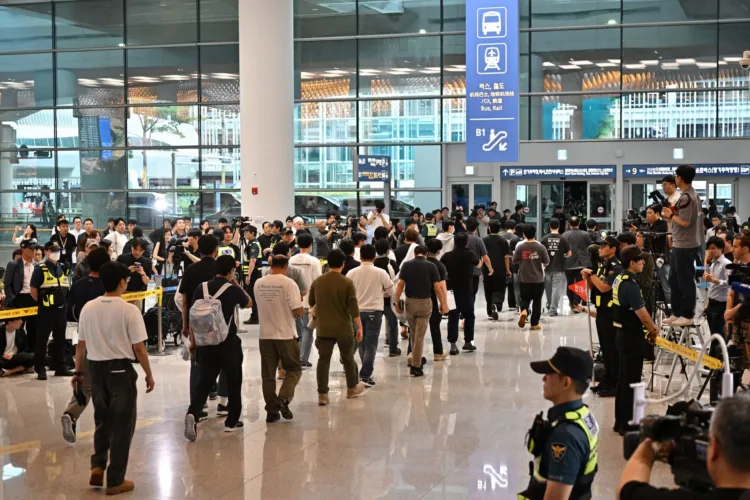 Una fila de hombres caminando por un aeropuerto, flanqueada por filas de oficiales de seguridad y fotógrafos. AFP