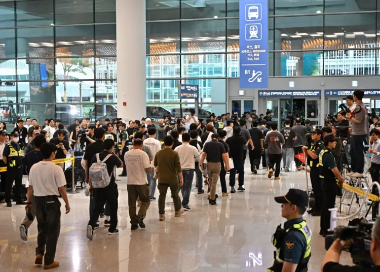 Una fila de hombres caminando por un aeropuerto, flanqueada por filas de oficiales de seguridad y fotógrafos. AFP