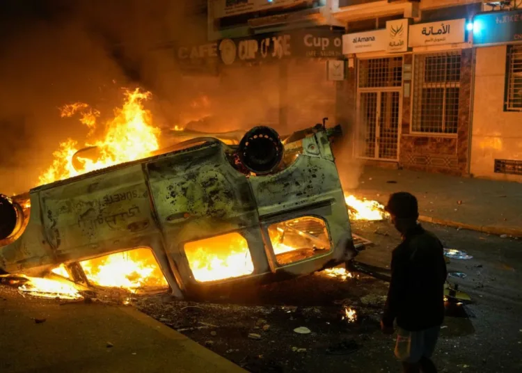 Un niño junto a un vehículo policial incendiado durante las violentas protestas lideradas por jóvenes en demanda de reformas sanitarias y educativas en Sale, Marruecos, el miércoles 1 de octubre de 2025. (AP Photo/Mosa'ab Elshamy)