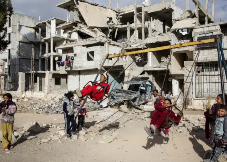 Niños juegan en una plaza que fue bombardeada anteriormente por las fuerzas del régimen en el campo de refugiados de Yarmouk, en Damasco, el 26 de diciembre. [Ali Haj Suleiman/Al Jazeera]