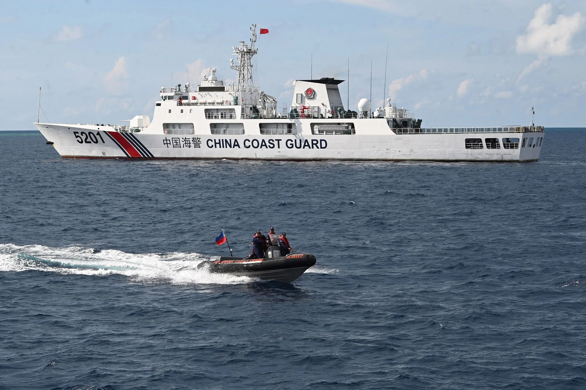 Personal del Servicio de Guardacostas de Filipinas en un bote inflable pasando rápidamente junto a un patrullero de la Guardia Costera de China cerca de un banco de arena disputado en el Mar del Sur de China en abril. Crédito... Ted Aljibe/Agence France-Presse — Getty Images
