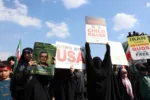 Una mujer sostiene un retrato de Alireza Tangsiri y carteles contra Estados Unidos durante su funeral. Créditos: AFP/ Aljazeera.