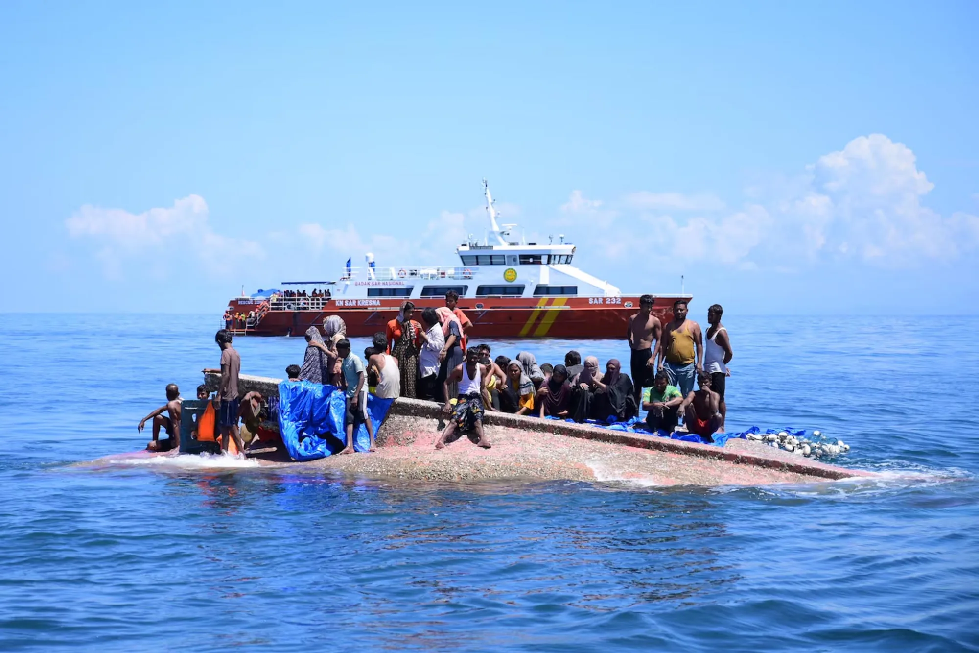 Unos refugiados rohingya se encuentran de pie sobre una embarcación volcada mientras una lancha de búsqueda y rescate indonesia se acerca para rescatarlos, en aguas de Aceh Occidental, Indonesia. Créditos: Reuters.