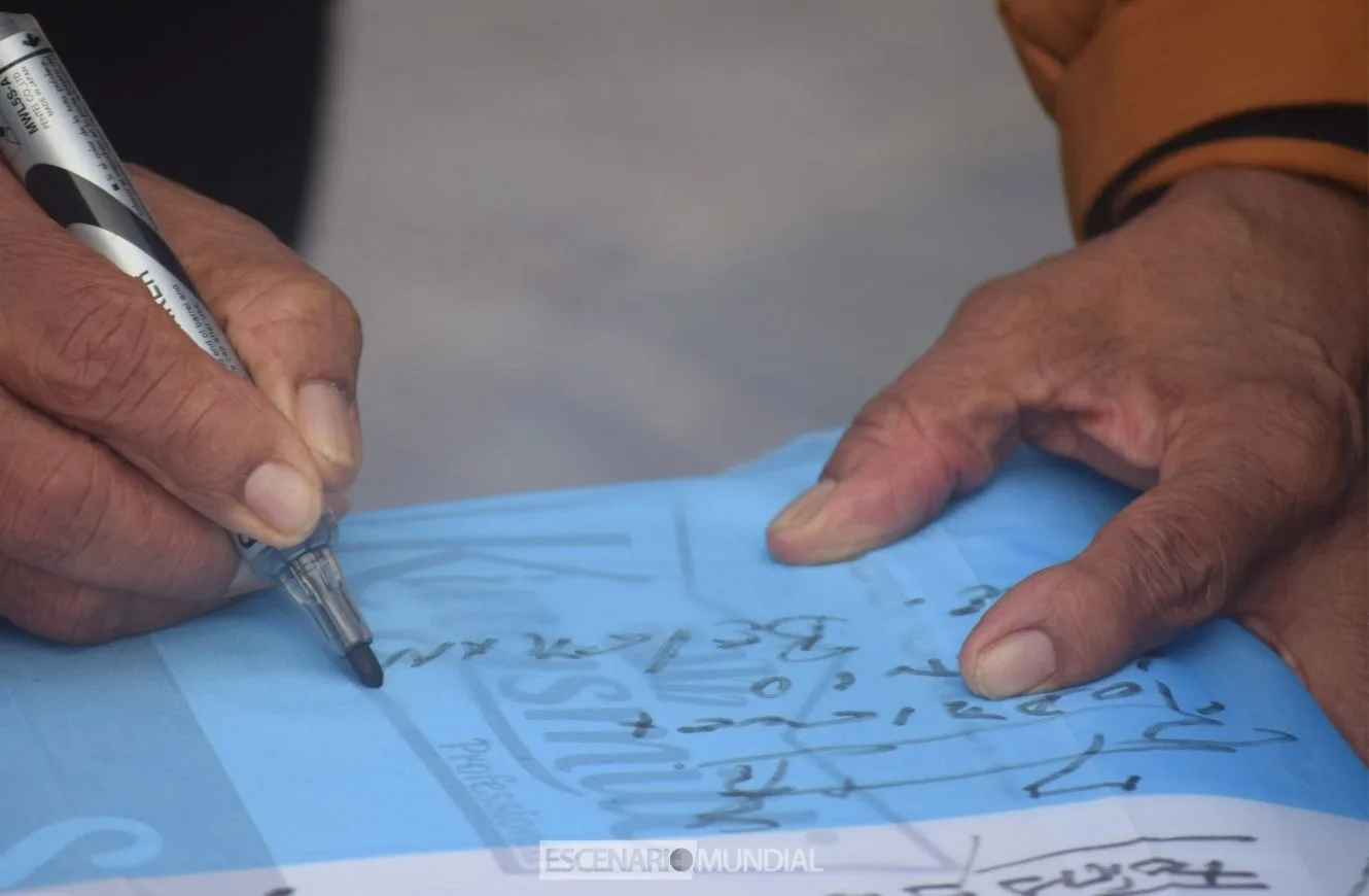 Hilario Rodriguez firma una bandera argentina que se dejó como recuerdo en el Cementerio de Darwin. Crédito: Alejo Sanchez Piccat / Escenario Mundial