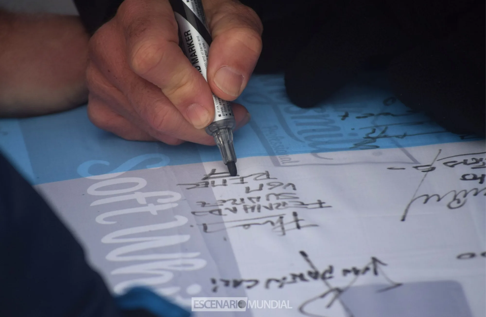 Fernando Suarez firma una bandera argentina que se dejó como recuerdo en el Cementerio de Darwin. Crédito: Alejo Sanchez Piccat / Escenario Mundial
