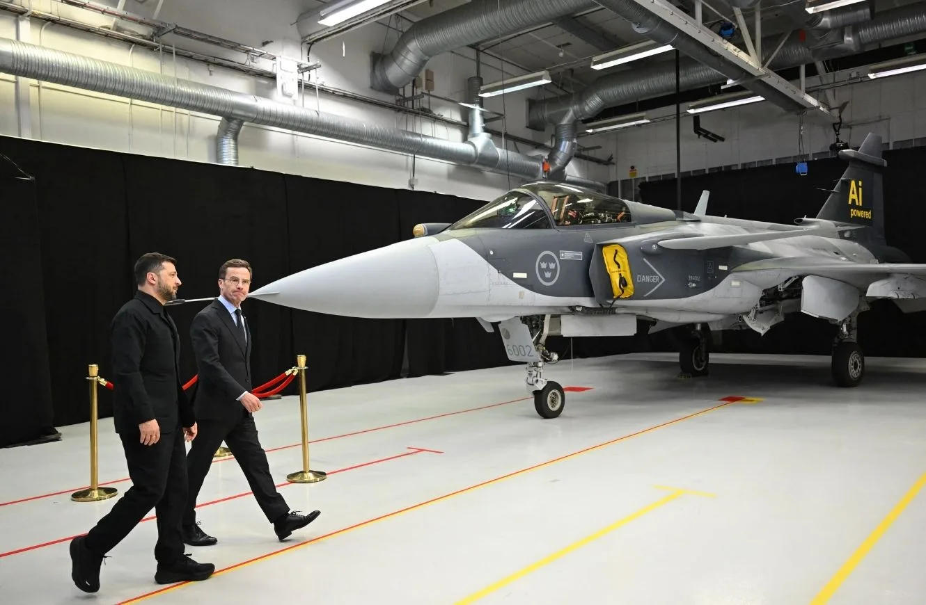 El primer ministro sueco Ulf Kristersson (R) y el presidente ucraniano Volodymyr Zelensky pasan junto a un avión de combate Gripen mientras llegan para ofrecer una conferencia de prensa conjunta en Linkoping, Suecia, el 22 de octubre de 2025. (Jonathan Nackstrand/AFP vía Getty Images)