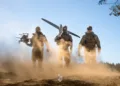 Soldados ucranianos equipados con drones (uno multicóptero y uno de ala fija) avanzando en un entorno polvoriento, subrayando capacidades modernas de combate. Créditos: Ministerio de Defensa de Ucrania.