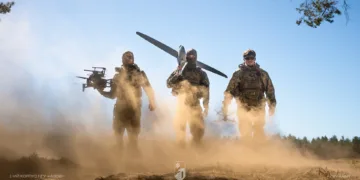 Soldados ucranianos equipados con drones (uno multicóptero y uno de ala fija) avanzando en un entorno polvoriento, subrayando capacidades modernas de combate. Créditos: Ministerio de Defensa de Ucrania.