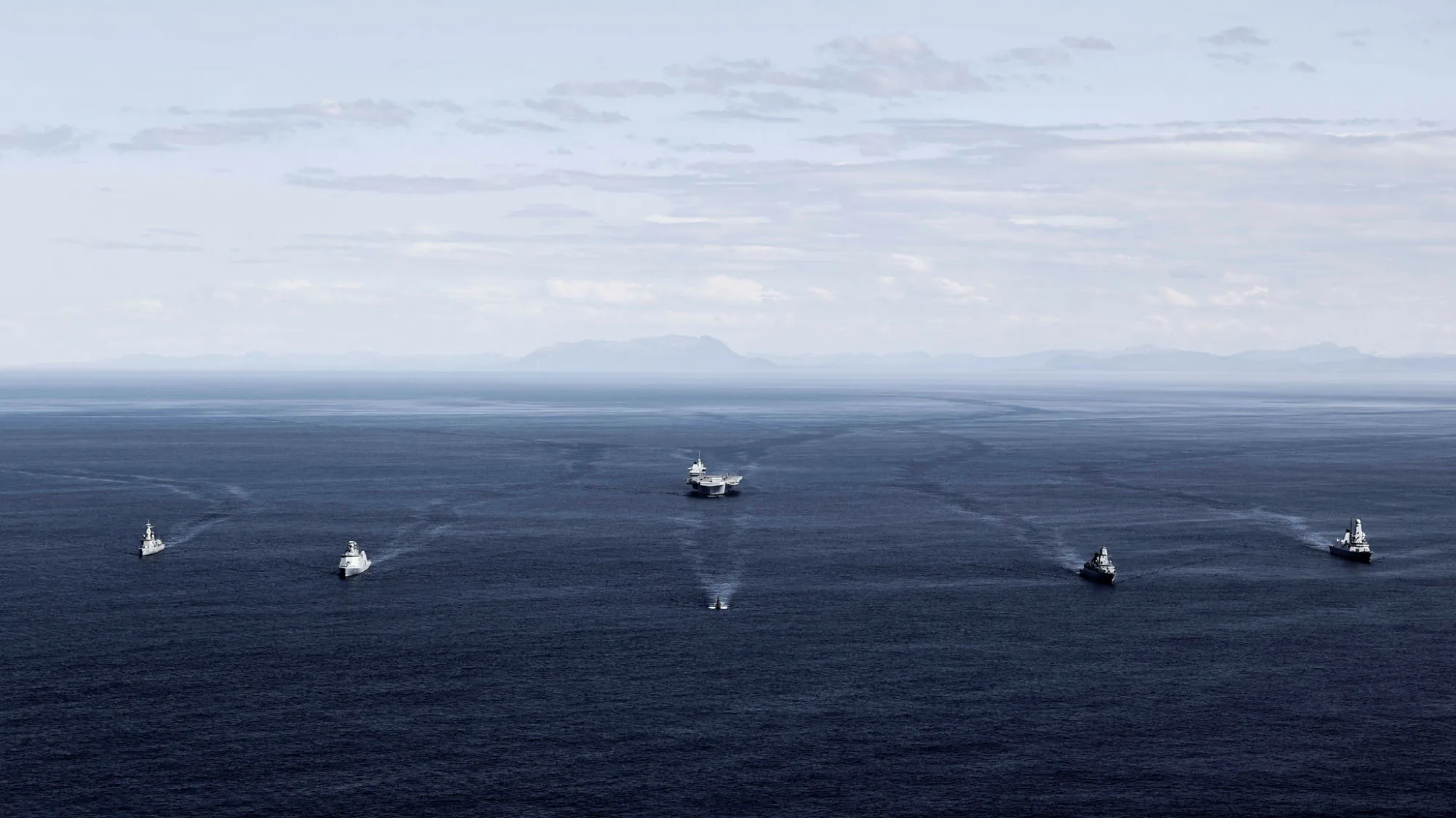 PHOTEX con el portaaviones HMS Prince of Wales (Reino Unido) como buque central. Alrededor de él, en formación de “estrella” o abanico con estelas visibles, navegan varios buques de superficie de la SNMG1 (Standing NATO Maritime Group 1) y participantes del ejercicio. Entre ellos: HMS Duncan (Reino Unido), FGS Sachsen (Alemania), HDMS Esbern Snare (Dinamarca) y unidades de Portugal (como NRP Francisco de Almeida), Países Bajos y posiblemente otras aliadas. Créditos: NATO Maritime Command.
