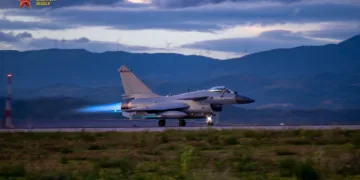 Un caza J-10 despegando en pista con postquemador encendido (llama azul), fondo montañoso con turbinas eólicas. Pertenece a una brigada de aviación de la Fuerza Aérea del Comando Sur del EPL. Créditos: China Military Bugle.