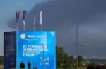 Agentes de policía se encuentran frente a un cartel y banderas con el logotipo del Foro Económico Internacional de San Petersburgo (SPIEF), mientras una densa humareda se eleva al fondo tras el impacto de drones en infraestructura, según informó el gobernador Alexander Beglov, en San Petersburgo, Rusia, el 3 de junio de 2026. REUTERS/Stringer