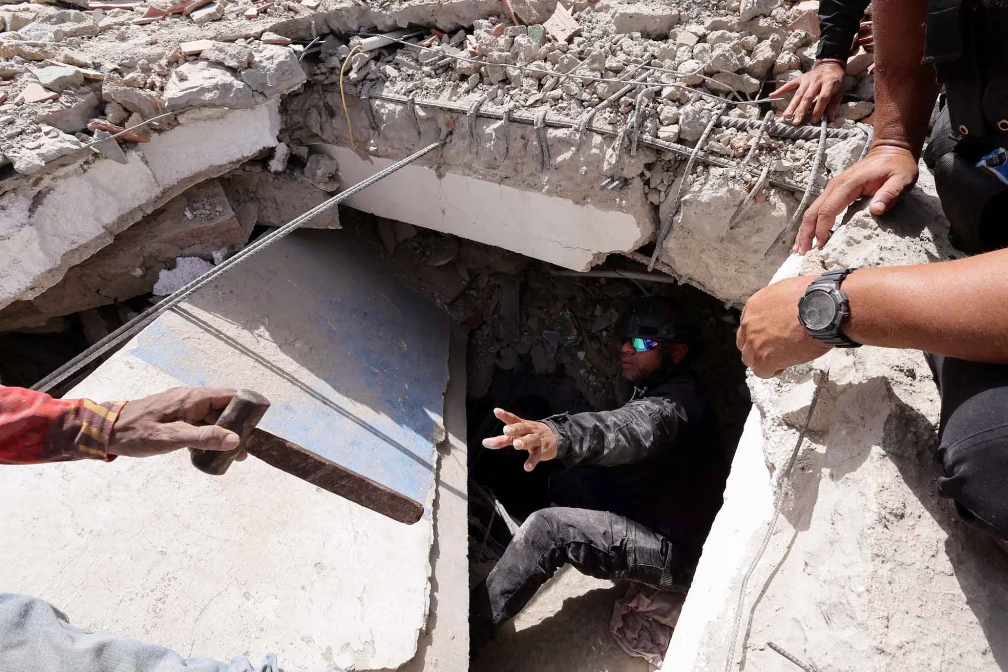 Una persona le entrega un martillo a un hombre mientras registran los escombros de un edificio en La Guaira, Venezuela, el 25 de junio. Créditos: Reuters.