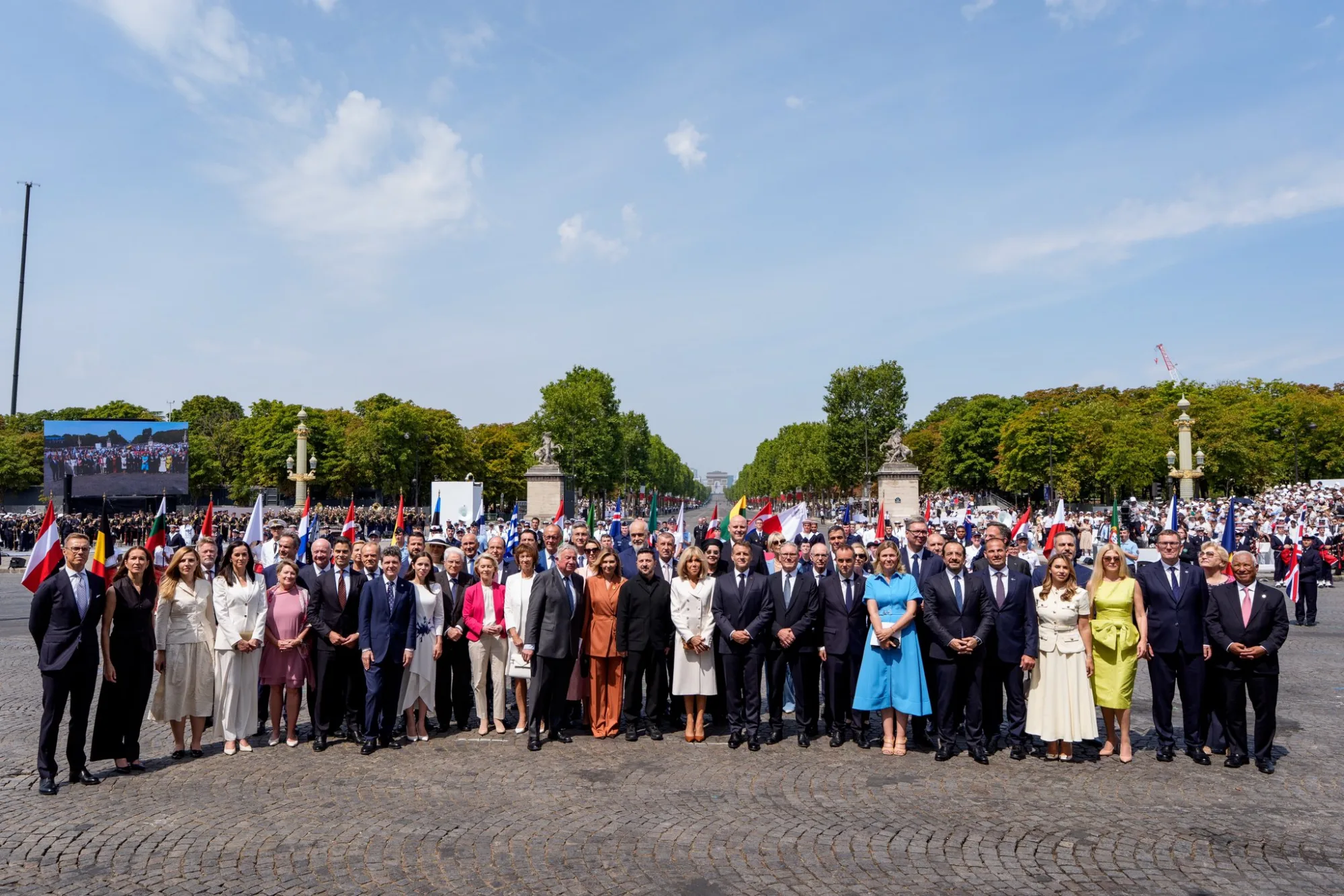 Emmanuel Macron muestra una gran foto grupal de líderes internacionales en los Campos Elíseos de París durante el Desfile del Día de la Bastilla 2026, acompañado del mensaje "Unis." para resaltar la unidad. Créditos: Emmanuel Macron.