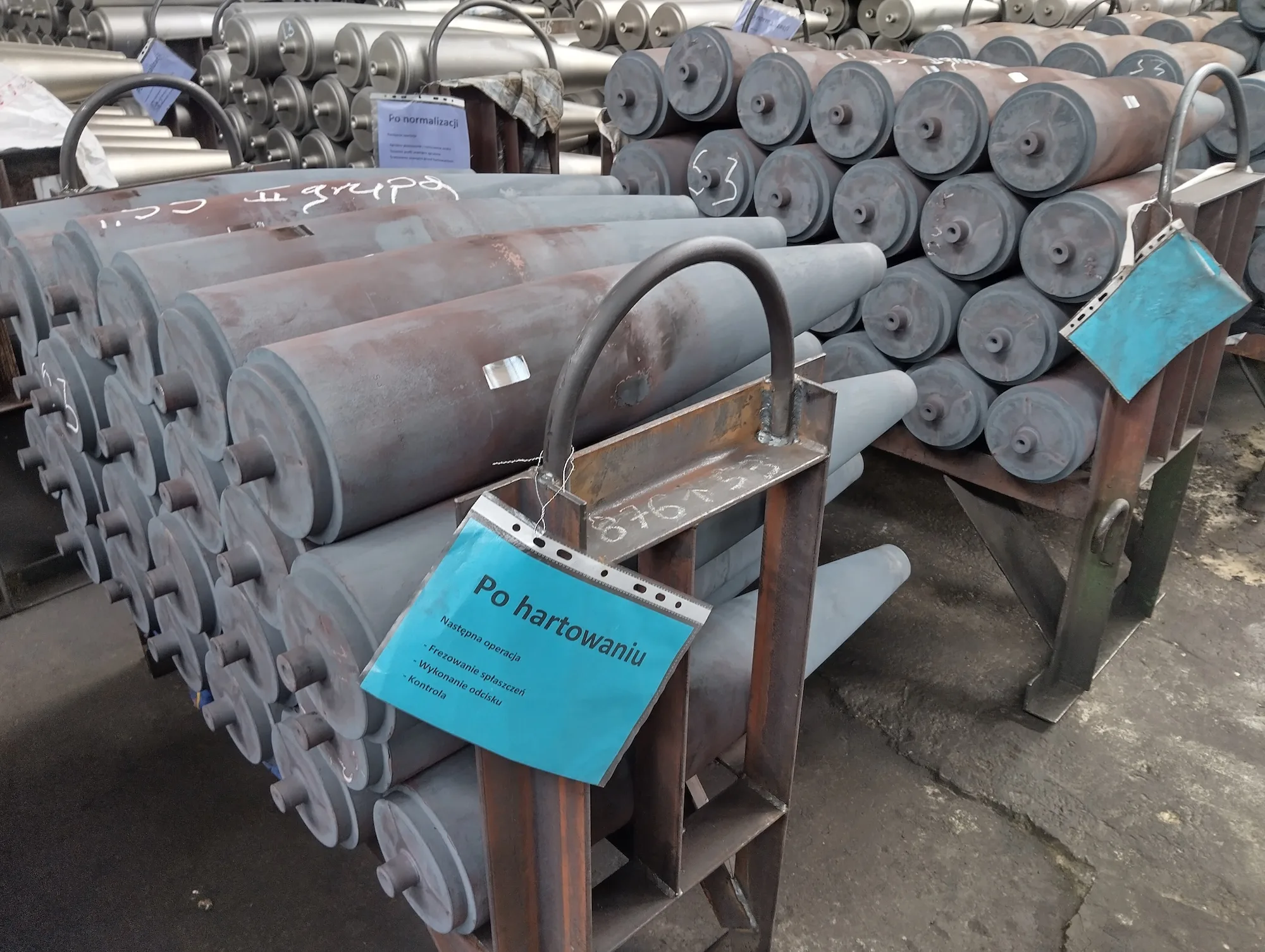 Casquillos para proyectiles de artillería apilados en racks industriales, con etiquetas en polaco como "Po hartowaniu" (después del endurecimiento), indicando etapas de procesamiento en la planta de MESKO. Créditos: Defence24.