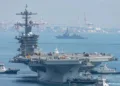 El portaaviones de propulsión nuclear USS George Washington navega frente a una zona portuaria, acompañado por embarcaciones de apoyo, en el Pacífico