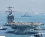 El portaaviones de propulsión nuclear USS George Washington navega frente a una zona portuaria, acompañado por embarcaciones de apoyo, en el Pacífico