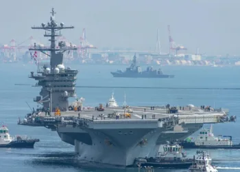 El portaaviones de propulsión nuclear USS George Washington navega frente a una zona portuaria, acompañado por embarcaciones de apoyo, en el Pacífico