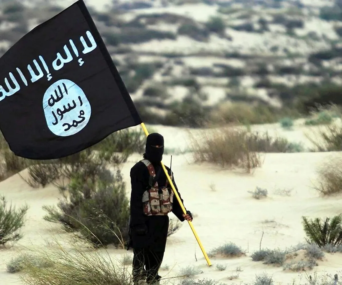 Un combatiente enmascarado posando en el desierto, mientras sostiene la bandera del Estado Islámico en Irak y Siria (ISIS)